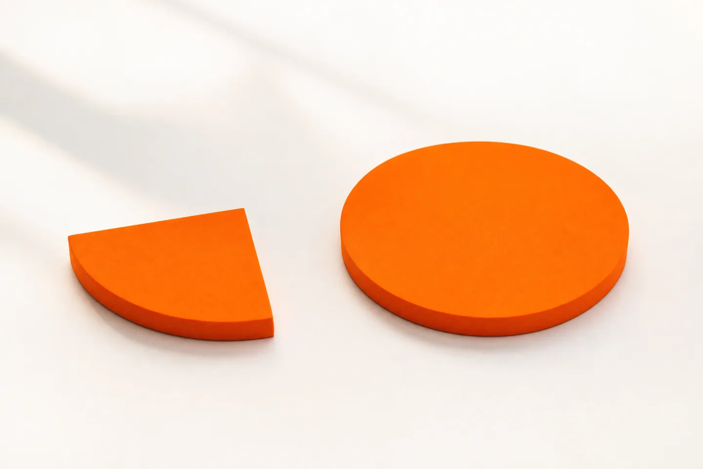 One quarter of a flat orange disc beside a whole orange disc on a white table